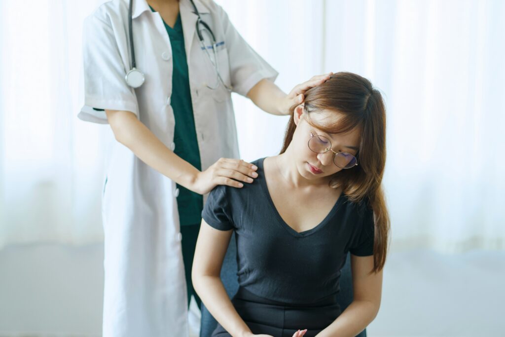 A woman sits on a chair as a doctor examines her back during a medical consultation.