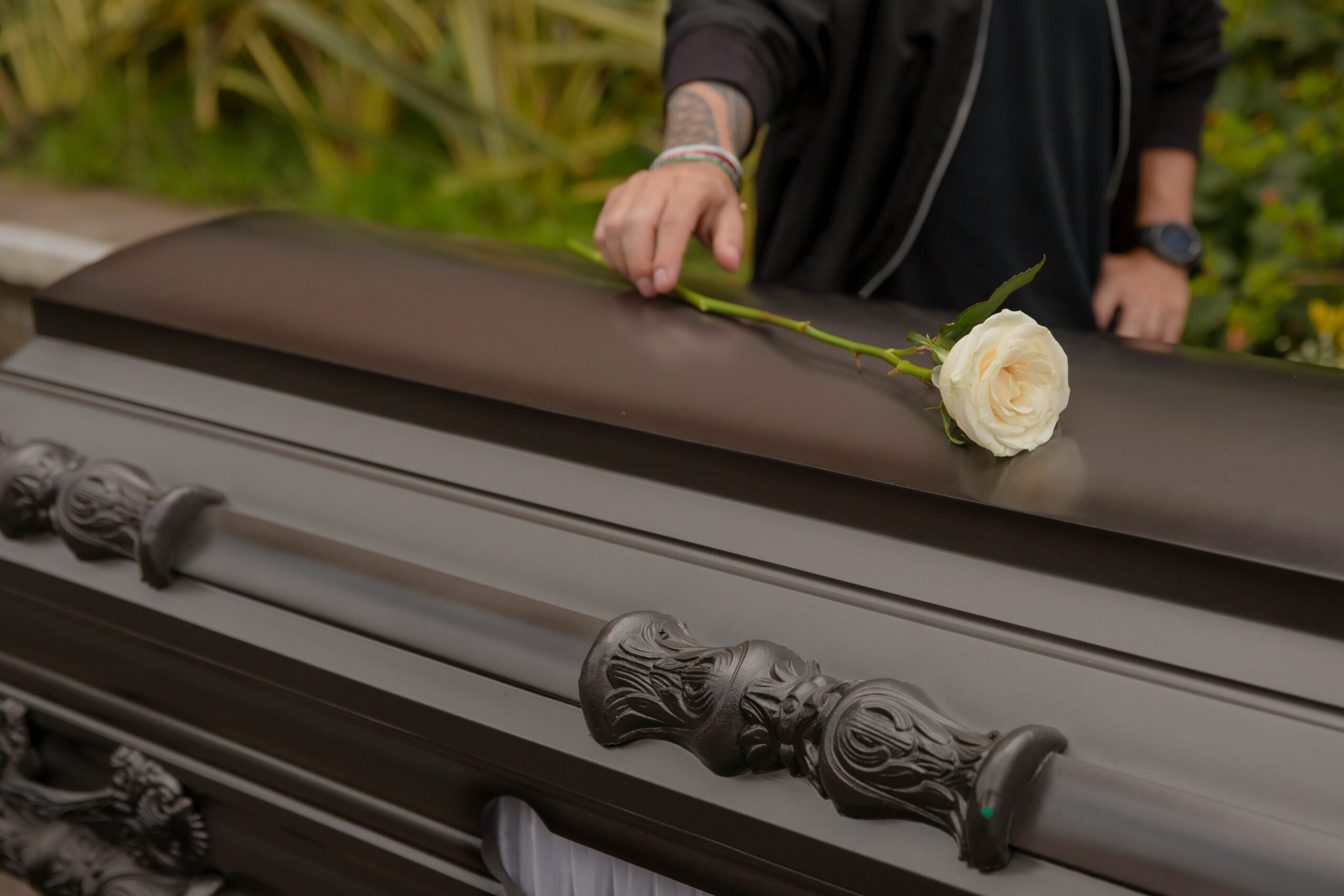 A person gently places a rose on a casket during a solemn memorial service.