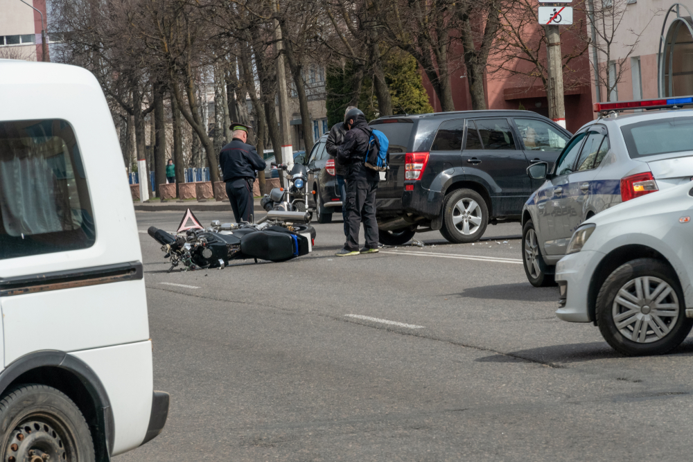 A white van parked near the scene of a motorcycle accident, with emergency responders attending to the situation.