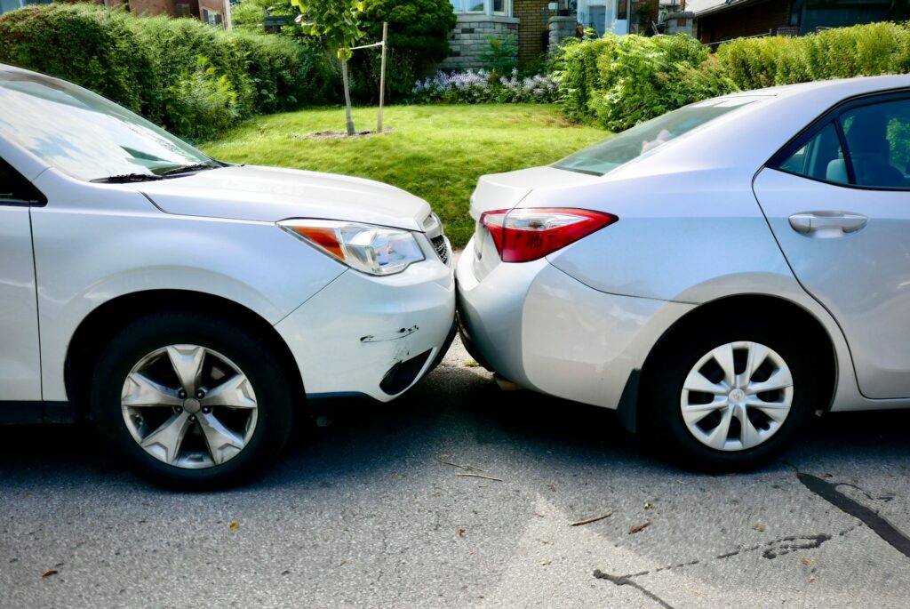 Two cars parked side by side in a residential driveway, surrounded by grass and a clear blue sky.